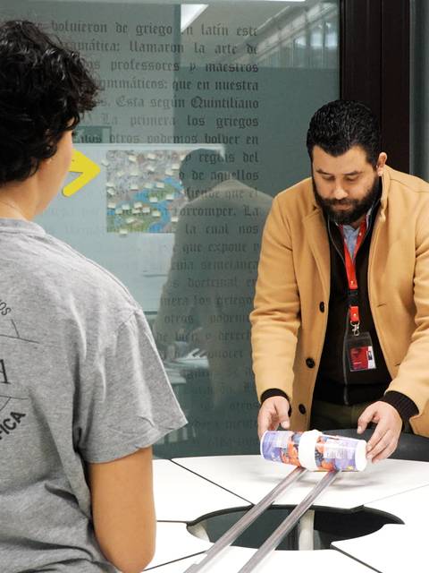 Un grupo de personas interactúa en un entorno de aprendizaje donde un hombre está mostrando un objeto sobre una mesa.