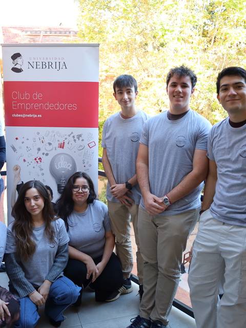 Un grupo de estudiantes está posando frente a un banner del Club de Emprendedores de la Universidad Nebrija.
