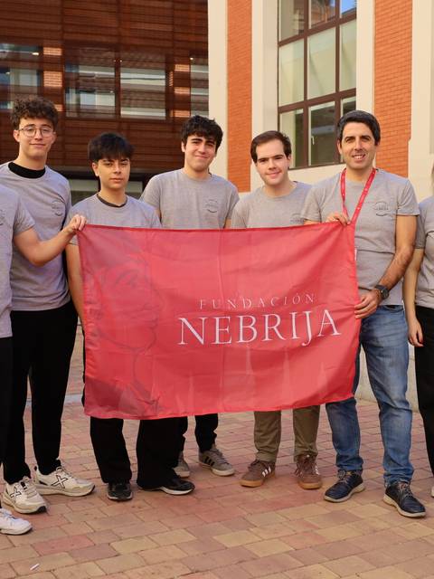 Grupo de personas posando con una bandera de la Fundación Nebrija en un ambiente al aire libre.