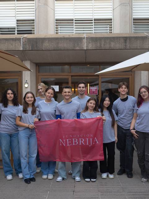 Grupo de estudiantes de pie, sosteniendo una bandera de la Universidad Nebrija en un lugar al aire libre.