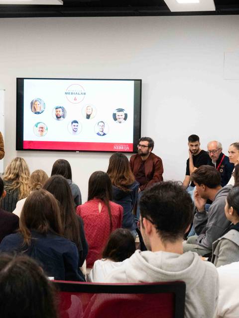 Una presentación en un espacio académico con un ponente frente a un público atento.