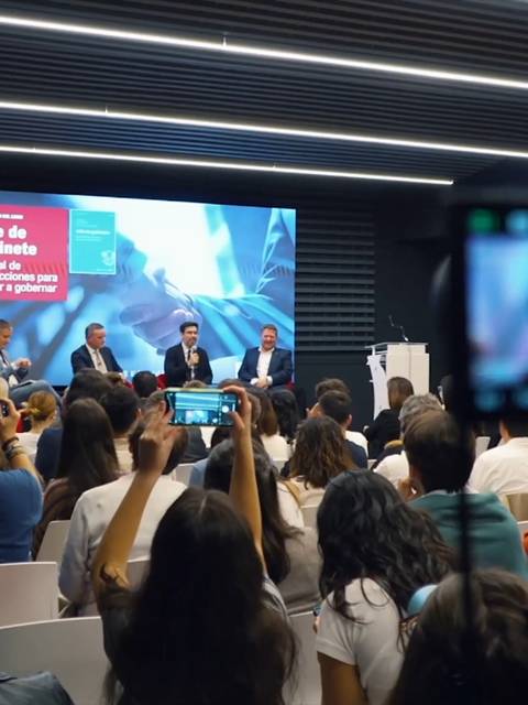 Una conferencia con un panel de expertos frente a una audiencia diversa en un ambiente moderno.