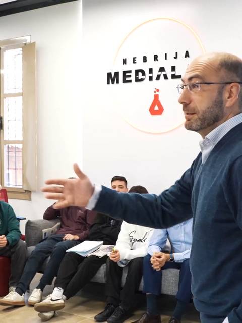 Un profesor está impartiendo una clase a un grupo de estudiantes en un ambiente educativo moderno.
