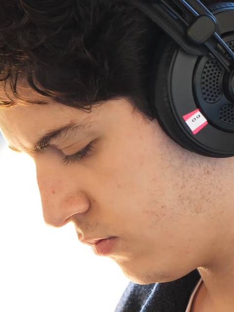 Un joven escucha música con auriculares mientras mira hacia abajo.