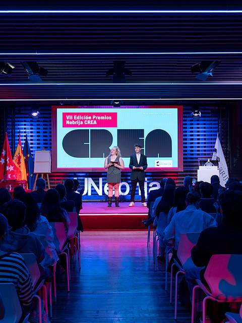 Un evento en el que se presentan oradores frente a un público, con pantallas y banderas visibles en el escenario.