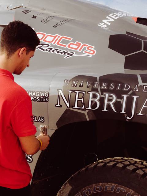 Un joven con camiseta roja trabaja en un vehículo de carreras que tiene publicidad de la Universidad Nebrija.