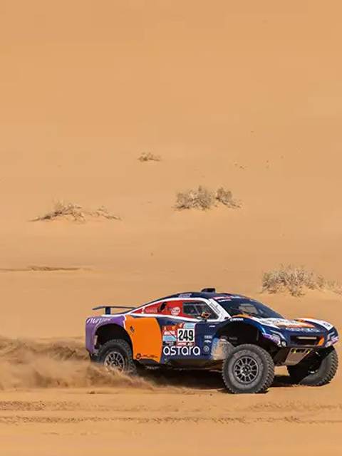 Un vehículo de carreras off-road corriendo por un desierto arenoso.