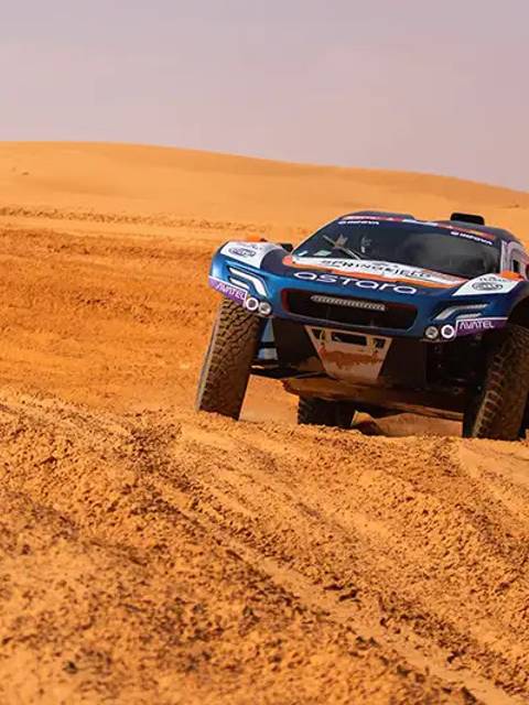 Un vehículo de carreras todoterreno surca un desierto con grandes dunas de arena.