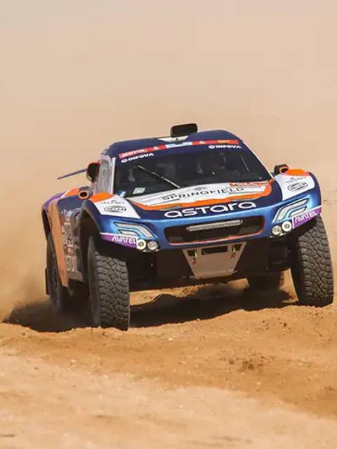 Un automóvil de carreras especializado en terrenos áridos derrapando en una pista de arena.