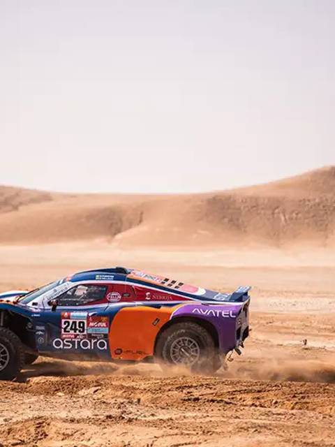 Un coche de rally compitiendo en un desierto polvoriento, levantando polvo a su paso.