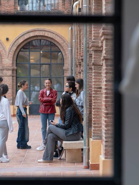 Un grupo de personas conversando en un patio interior rodeado de arcos y ladrillos.