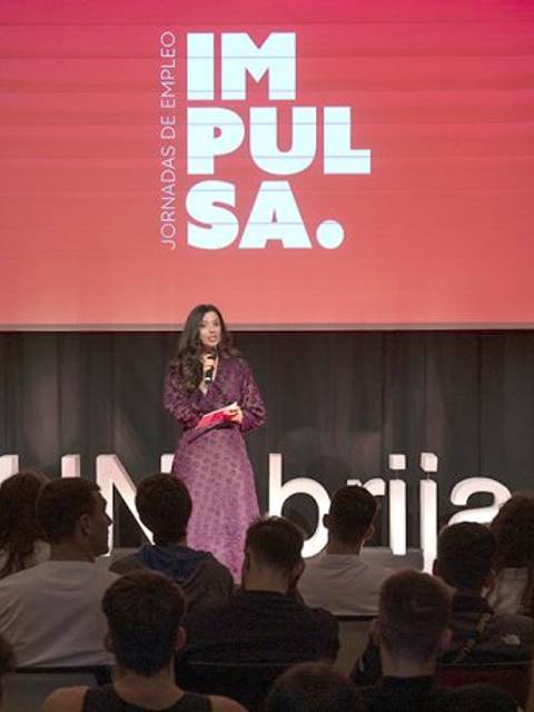 Un evento de jornadas de empleo donde una mujer presenta en el escenario frente a una audiencia.
