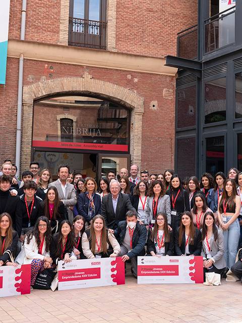 Un grupo de jóvenes se reúne frente a un edificio, todos vestidos con distintivos y sonriendo para la foto.