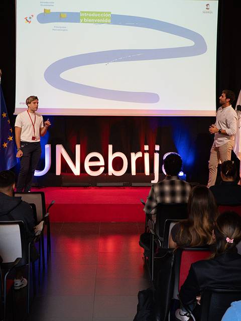 Una presentación en una conferencia con dos ponentes y un público atento.