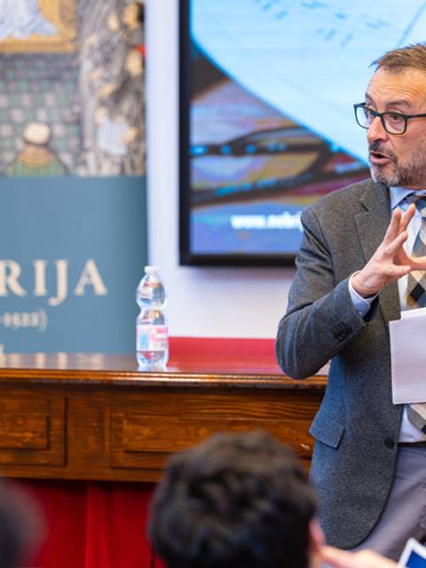 Un hombre está hablando en un evento mientras sostiene un papel y gesticula con la mano.