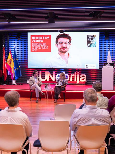 Un evento literario con un panel de discusión frente a una audiencia en un escenario bien iluminado.