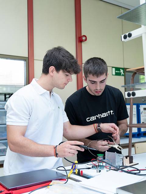 Dos estudiantes trabajan juntos en un laboratorio realizando un experimento con un dispositivo electrónico.