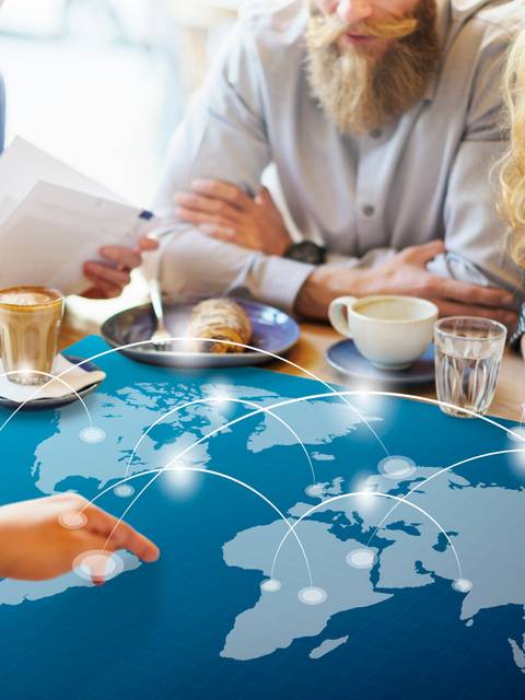 Un grupo de personas se reúne en una mesa con un mapa del mundo proyectado y varias tazas de café.