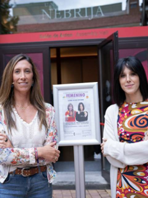 Dos mujeres posan junto a un cartel en la entrada de un edificio que lleva el nombre 'Nebrija'.