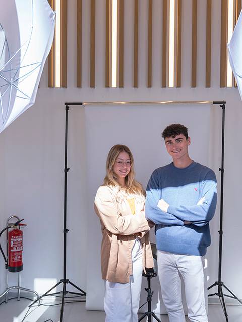 Dos personas posan frente a un fondo con iluminación profesional en un estudio fotográfico.