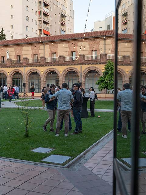 Un grupo de personas se reúne en un jardín mientras se reflejan los edificios en un vidrio.
