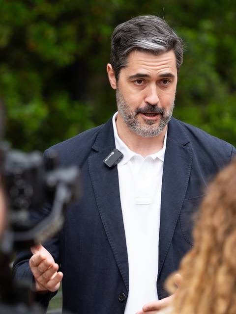 Un hombre habla ante una cámara mientras es entrevistado por un reportero.