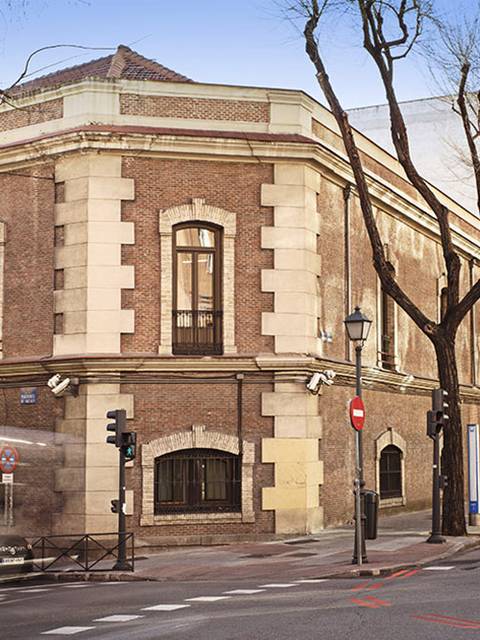 Edificio histórico en una esquina con árboles desnudos y tráfico en la calle.