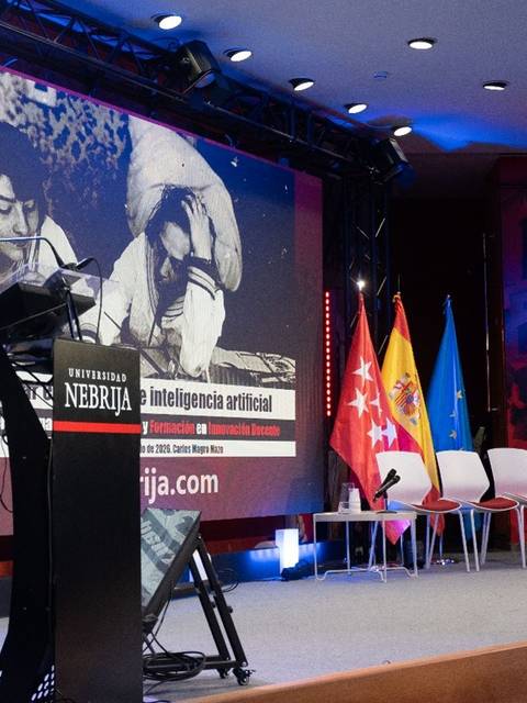 Un ponente habla sobre inteligencia artificial en un evento académico con pantallas y banderas al fondo.