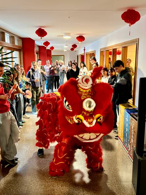 Un dragón rojo de danza tradicional avanza por un pasillo mientras la multitud lo observa y graba con sus teléfonos.