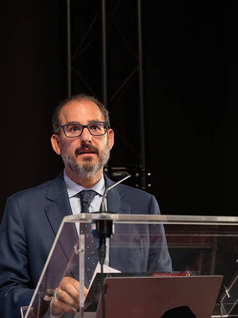 Un hombre de pie frente a un micrófono, dando una charla en un evento académico.