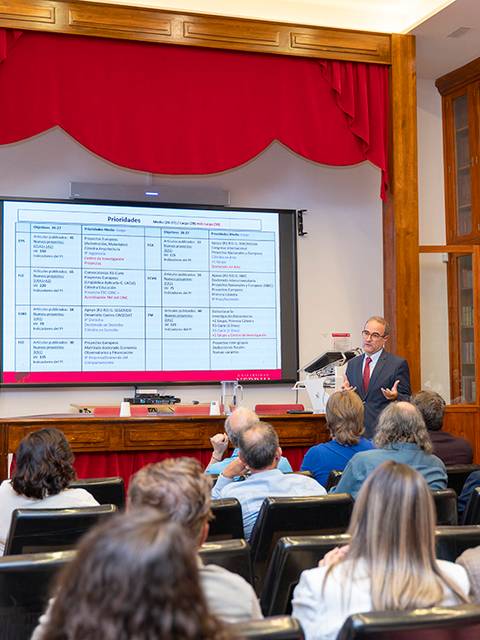 Un presentador expone información en una pantalla a un grupo de personas en un salón de eventos.