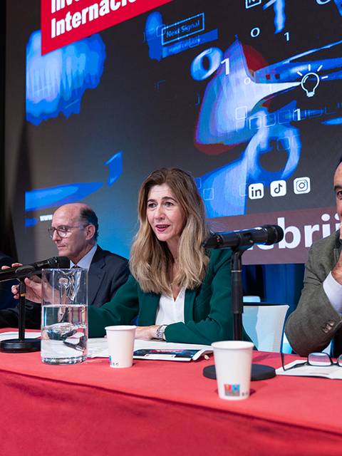 Cuatro personas sentadas en una mesa durante un evento con banderas de España y la Unión Europea de fondo.