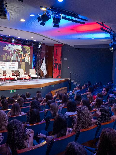Una sala llena de personas asistiendo a un evento con un escenario preparado para una presentación.