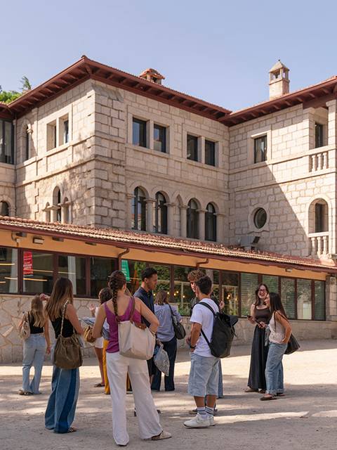 Un grupo de personas se reúne frente a un edificio de estilo arquitectónico clásico en un ambiente al aire libre.