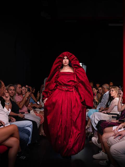 Una modelo desfila en una pasarela luciendo un vestido rojo en un ambiente de moda.