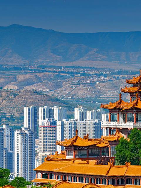 Una vista panorámica de un edificio tradicional con techos en punta frente a un paisaje urbano moderno y montañoso.