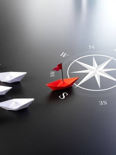 Una imagen que muestra varios barcos de papel blancos y uno rojo, junto a una brújula que indica direcciones cardinales.