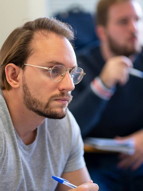 Un estudiante observa atentamente mientras toma notas en clase.