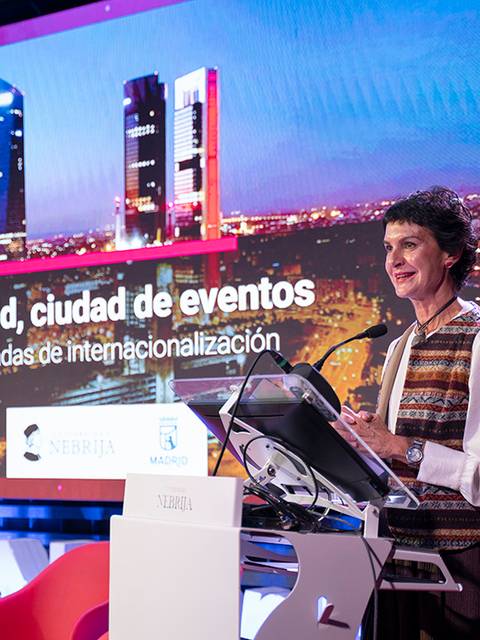 Una mujer habla en un evento en Madrid sobre la internacionalización, con un fondo de edificios emblemáticos de la ciudad.