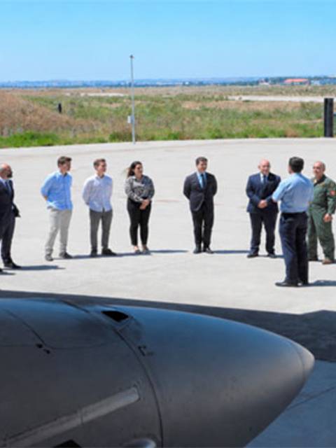 Un grupo de personas se reúne en una pista de aterrizaje al aire libre, conversando y observando un avión en primer plano
