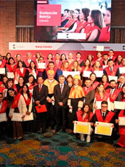 La imagen muestra a un grupo grande de graduados posando con sus certificados en un evento de graduación.