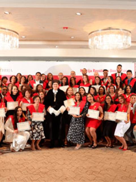 Un grupo de graduados posando felices con sus certificados en una ceremonia celebrada en un salón elegante.