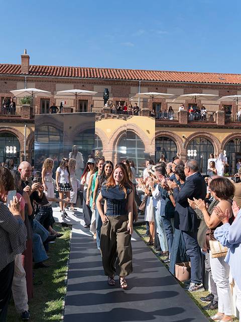 Un desfile de moda al aire libre con un público entusiasta aplaudiendo a las modelos que caminan por la pasarela.