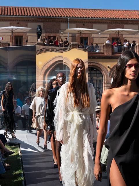 Un desfile de moda al aire libre con modelos caminando por la pasarela ante una audiencia atenta.