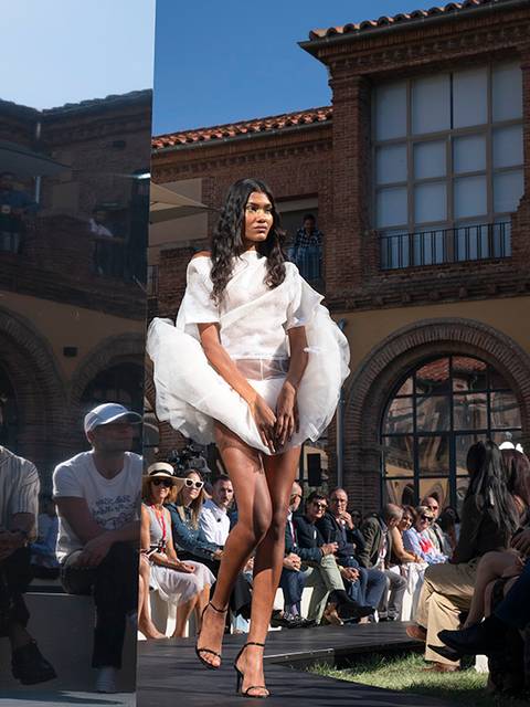 Una modelo camina con un atuendo elegante en una pasarela al aire libre frente a un público atento.