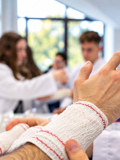 La imagen muestra a personas en un entorno de aprendizaje sobre vendajes y primeros auxilios.