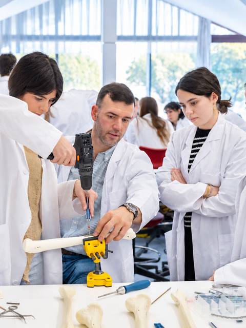 Un grupo de personas en un aula práctica de medicina manipulan un modelo óseo mientras un instructor guía la actividad.