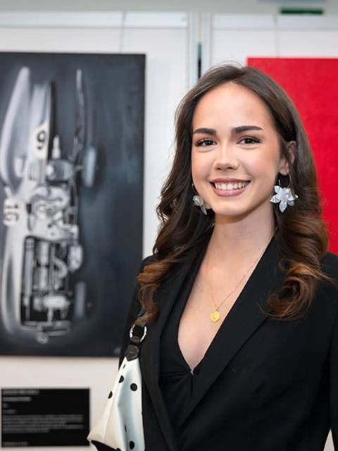 Una joven sonriente posa frente a obras de arte en una galería.