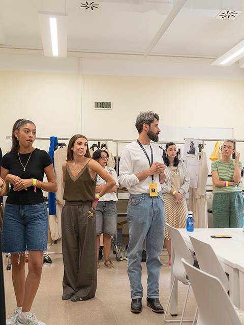 Un grupo de personas se reúne en un espacio de trabajo, observando y comentando sobre ropa y accesorios exhibidos.