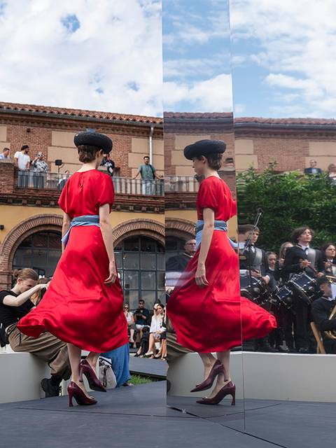 Una mujer con un vestido rojo camina frente a espejos en un evento al aire libre con una banda de música de fondo.